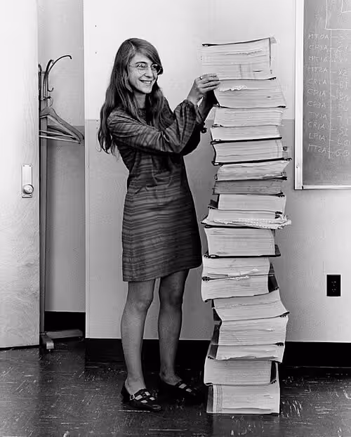 Margaret Hamilton standing beside printed Apollo guidance software code.
